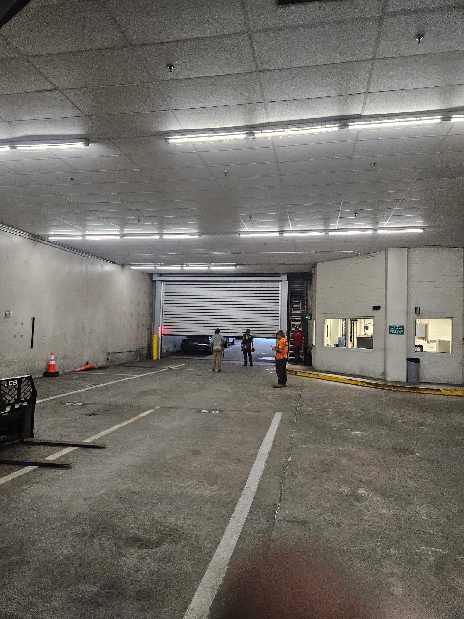 Warehouse interior with people near a loading door, lit by overhead fluorescent lights.