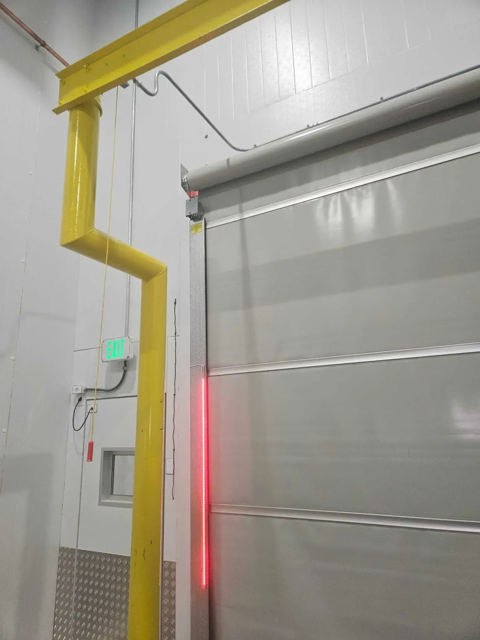 Automatic door with a red light sensor. Yellow support structure on a wall in a warehouse.