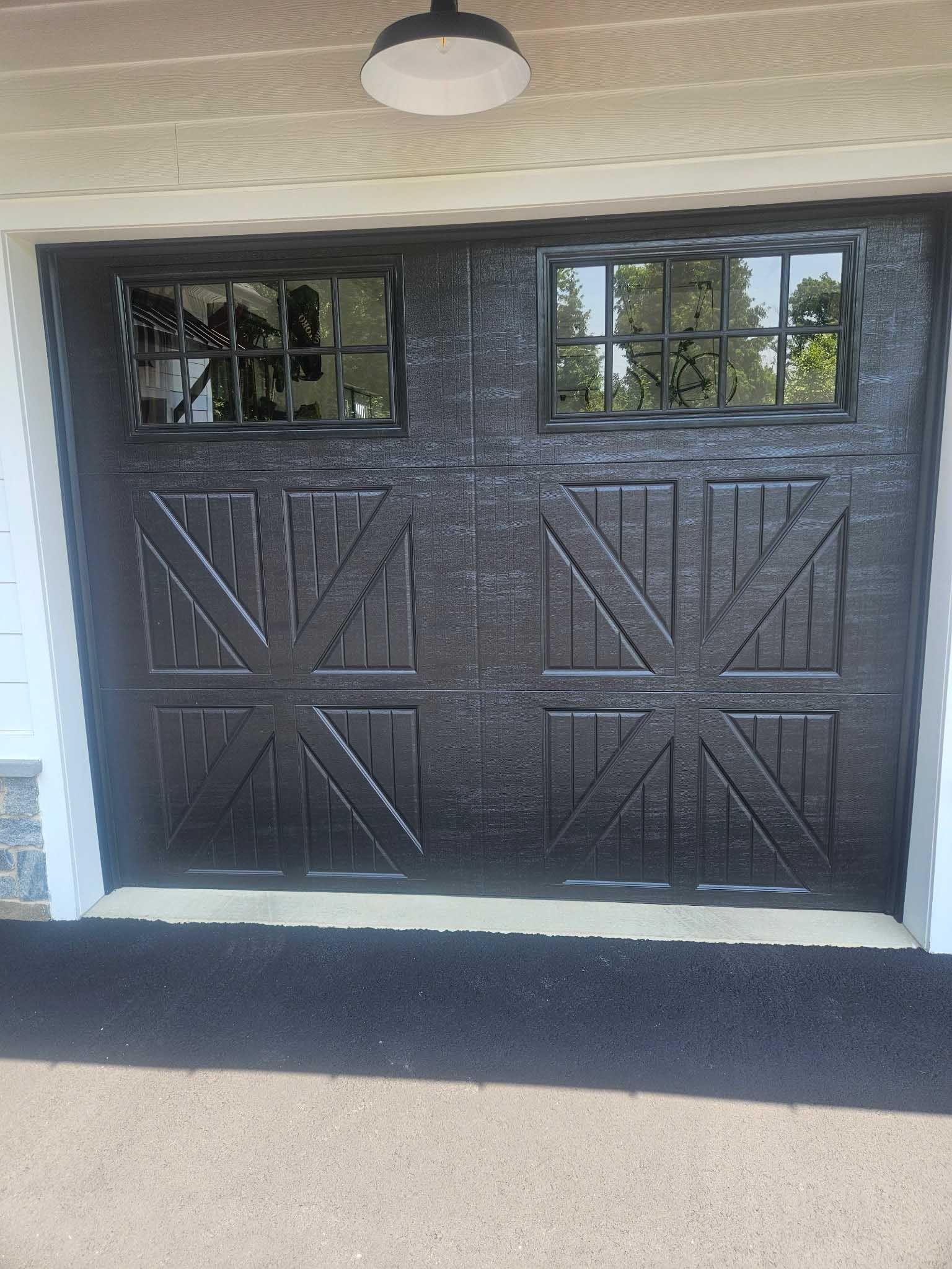 Black garage door with two square windows, textured with a cross pattern design.