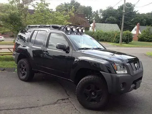 Black Nissan Xterra SUV with a roof rack and off-road lights, parked on a paved surface.