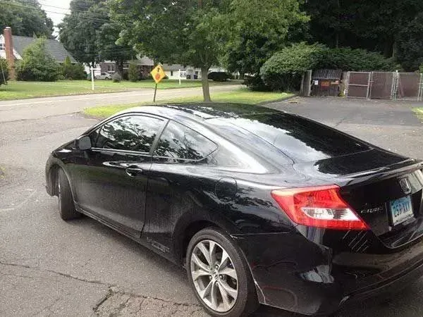 Black Honda Civic coupe parked on a paved driveway next to a grassy area with a tree.