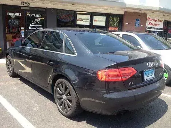 Black Audi A4 sedan parked outside of a storefront with signs.