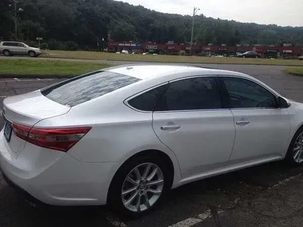 White Toyota Avalon sedan parked in a lot with green background and trees.