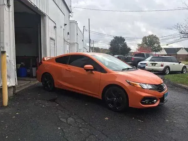 Orange Honda Civic coupe parked outside a garage with tinted windows and black wheels.