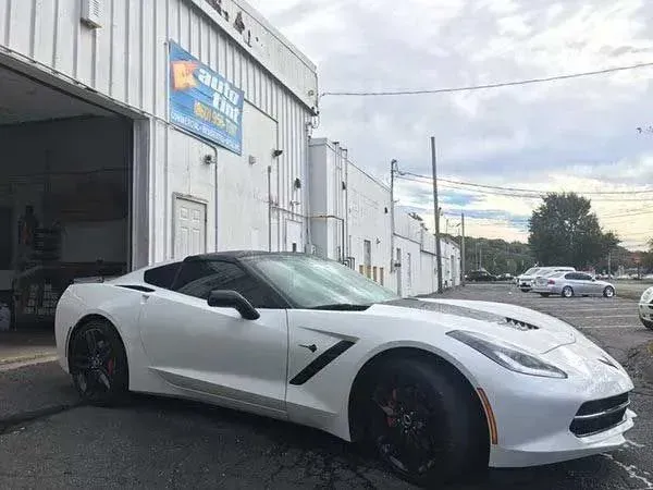 White Corvette in front of a garage with open bay door; sky in background.