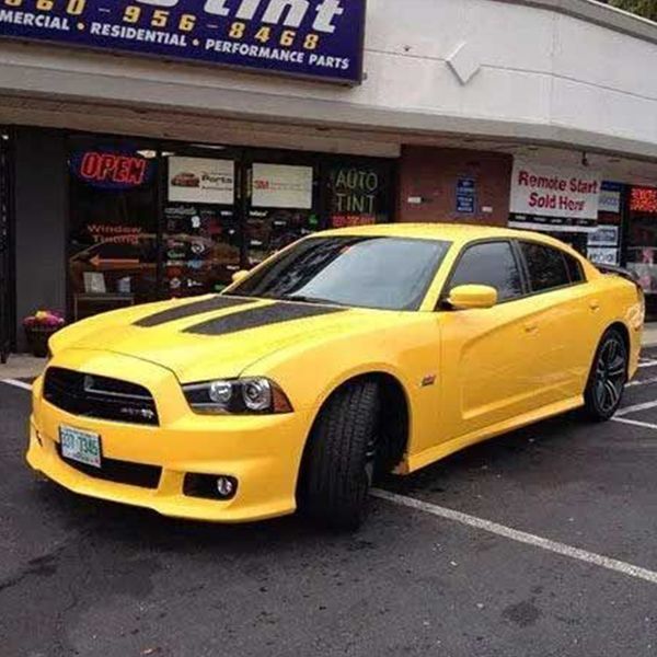 Yellow Dodge Charger with black stripes parked outside a tint shop.