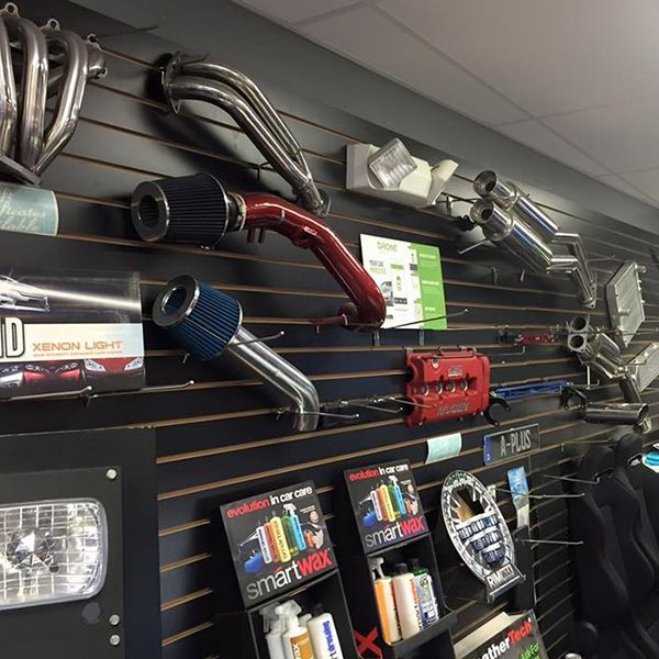 Car parts displayed on a black slat wall in a store. Includes exhaust systems, air filters, and SmartWax products.