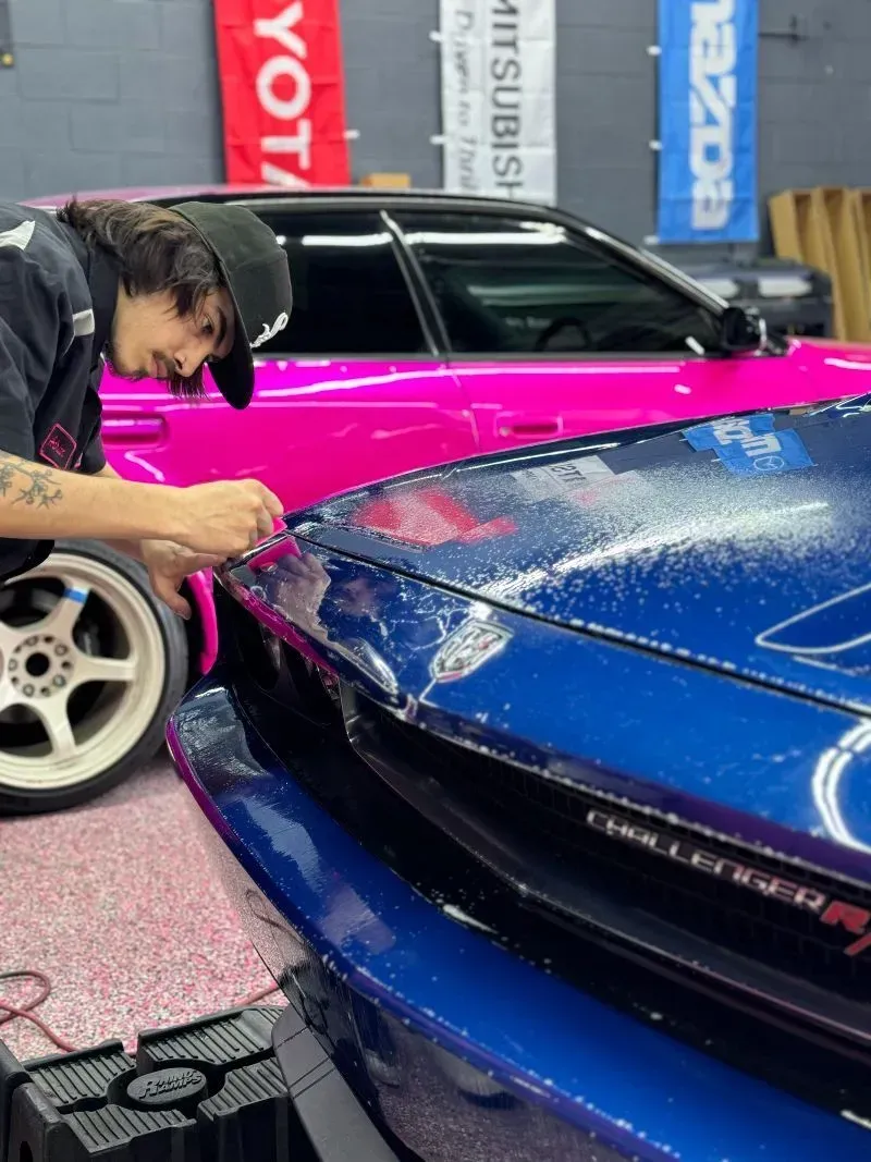 A man is working on a pink car and a blue car