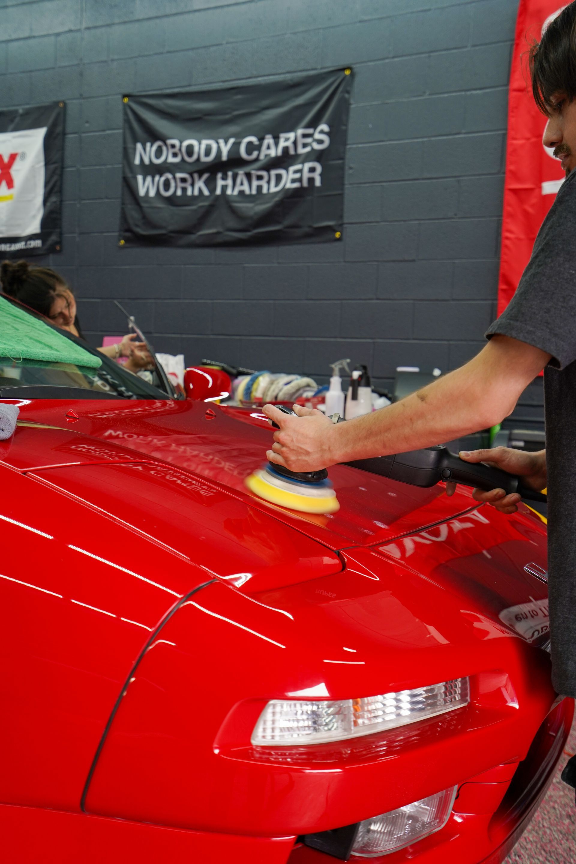 A man is polishing a red car in a garage.