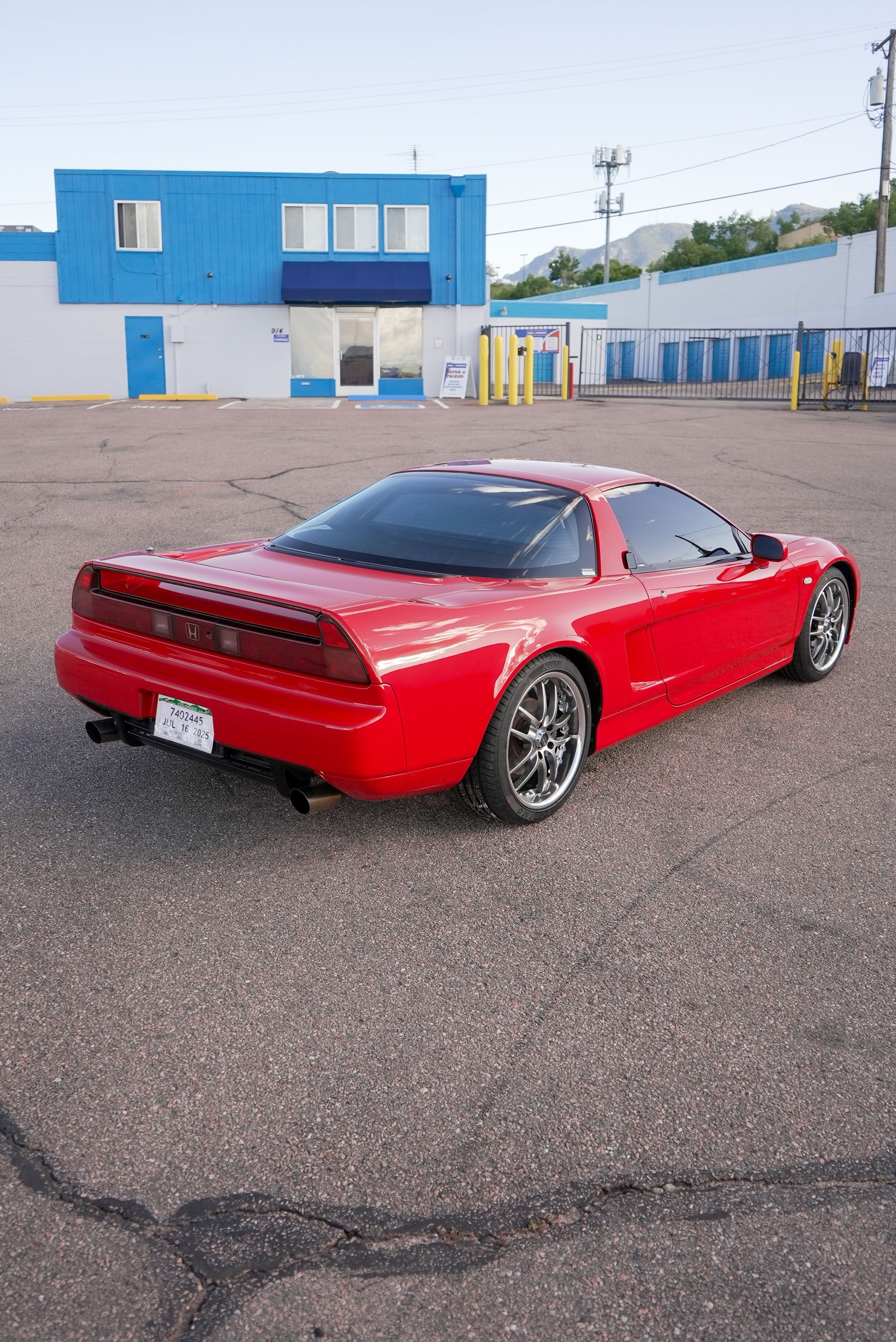 A red sports car is parked in a parking lot in front of a blue building.