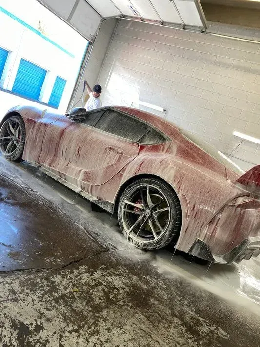 A red sports car is covered in foam at a car wash.