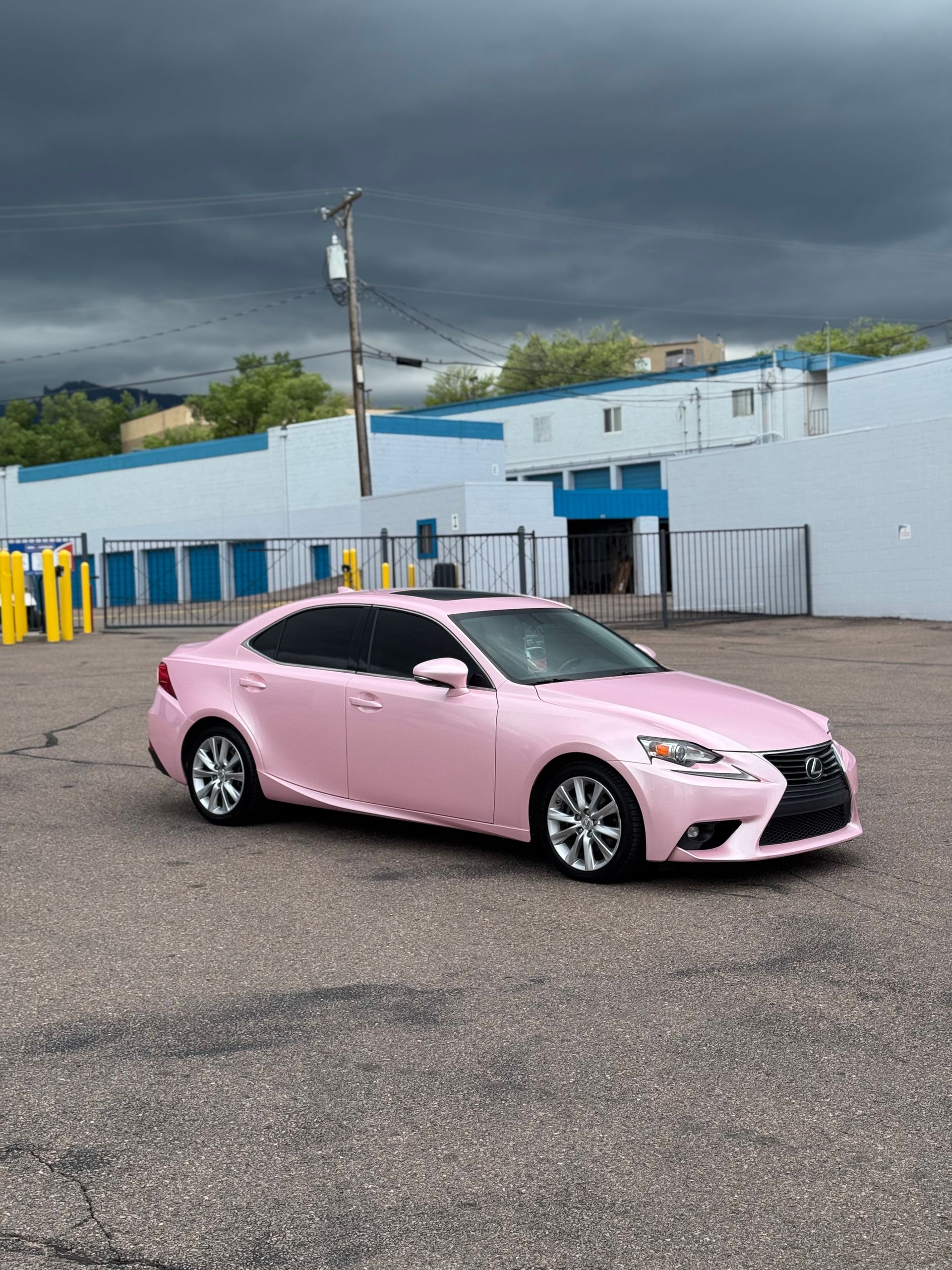 A pink car is parked in a parking lot in front of a building.