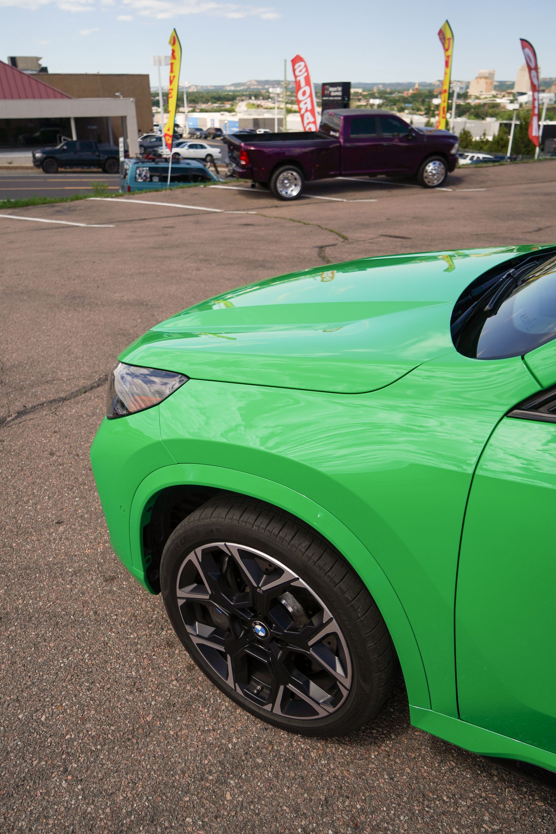 A green car is parked in a parking lot next to a truck.