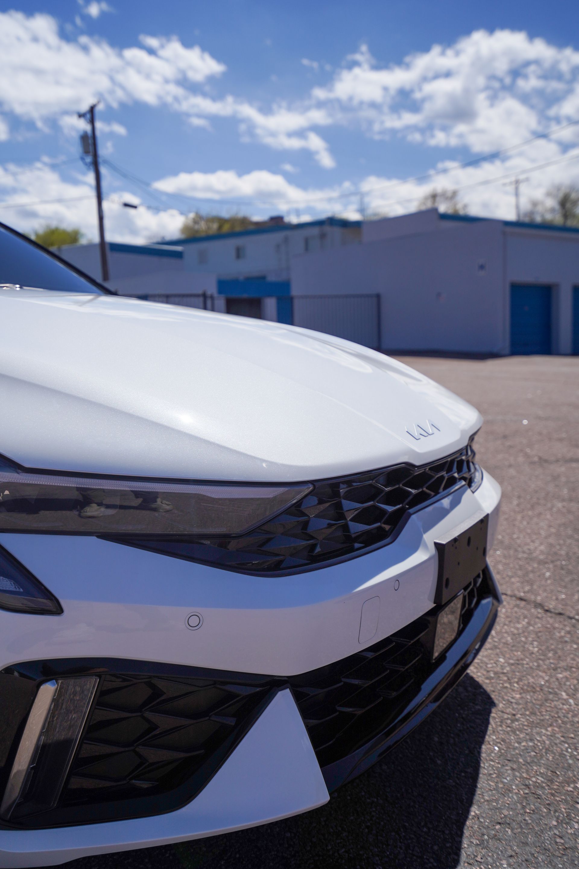 White Kia car's front, angled right, on a sunny day in a parking lot. Includes a grille and a partially visible license plate.