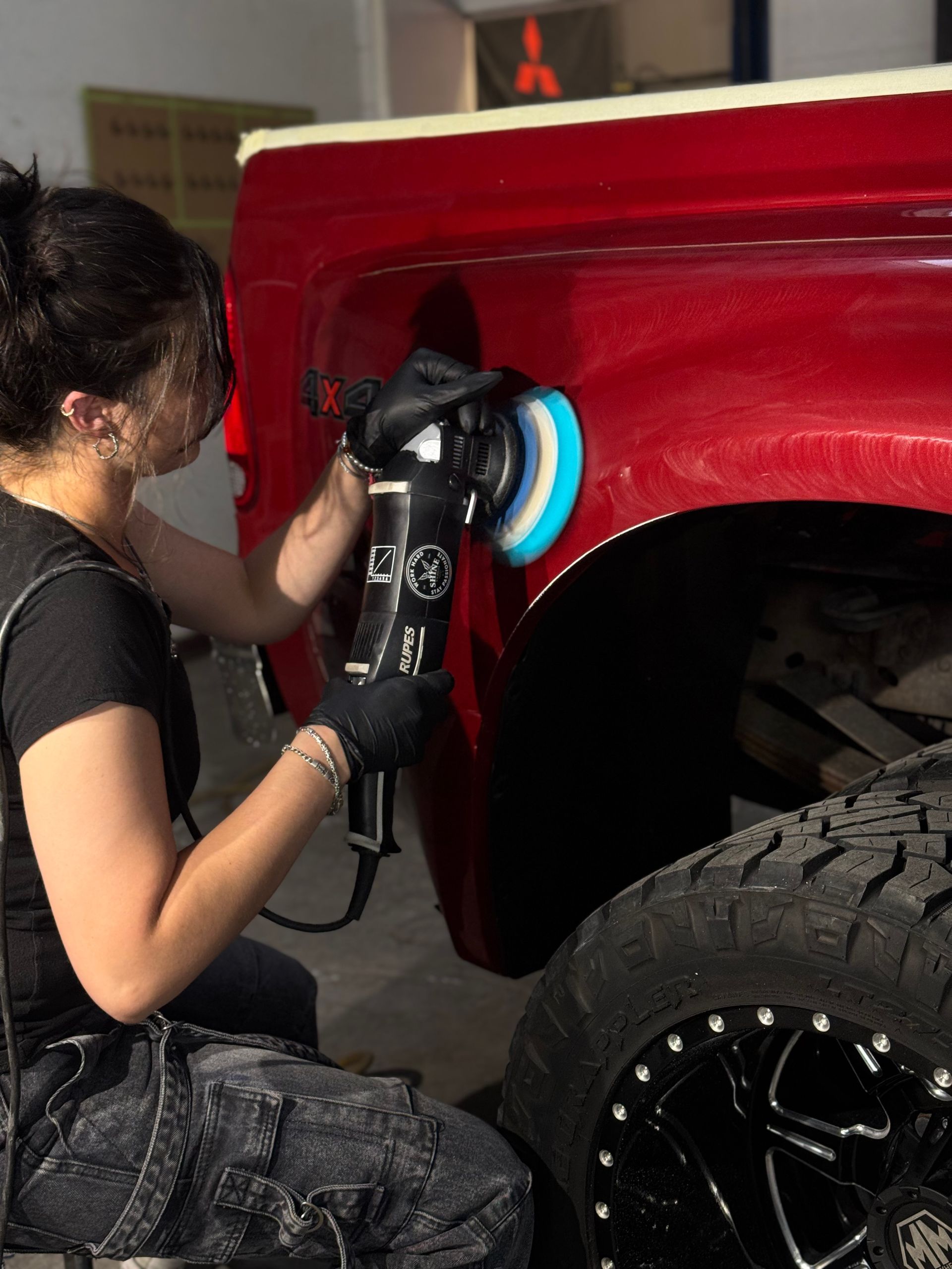 A woman is polishing the fender of a red truck