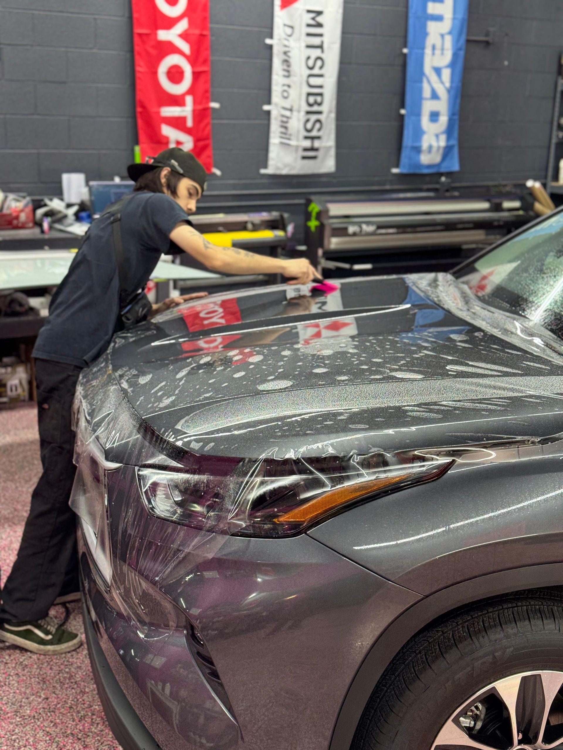 A man is working on the hood of a mazda car