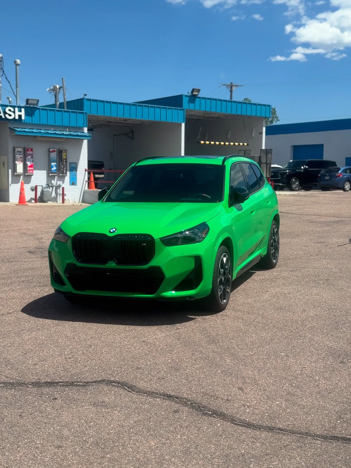 A green car is parked in front of a car wash