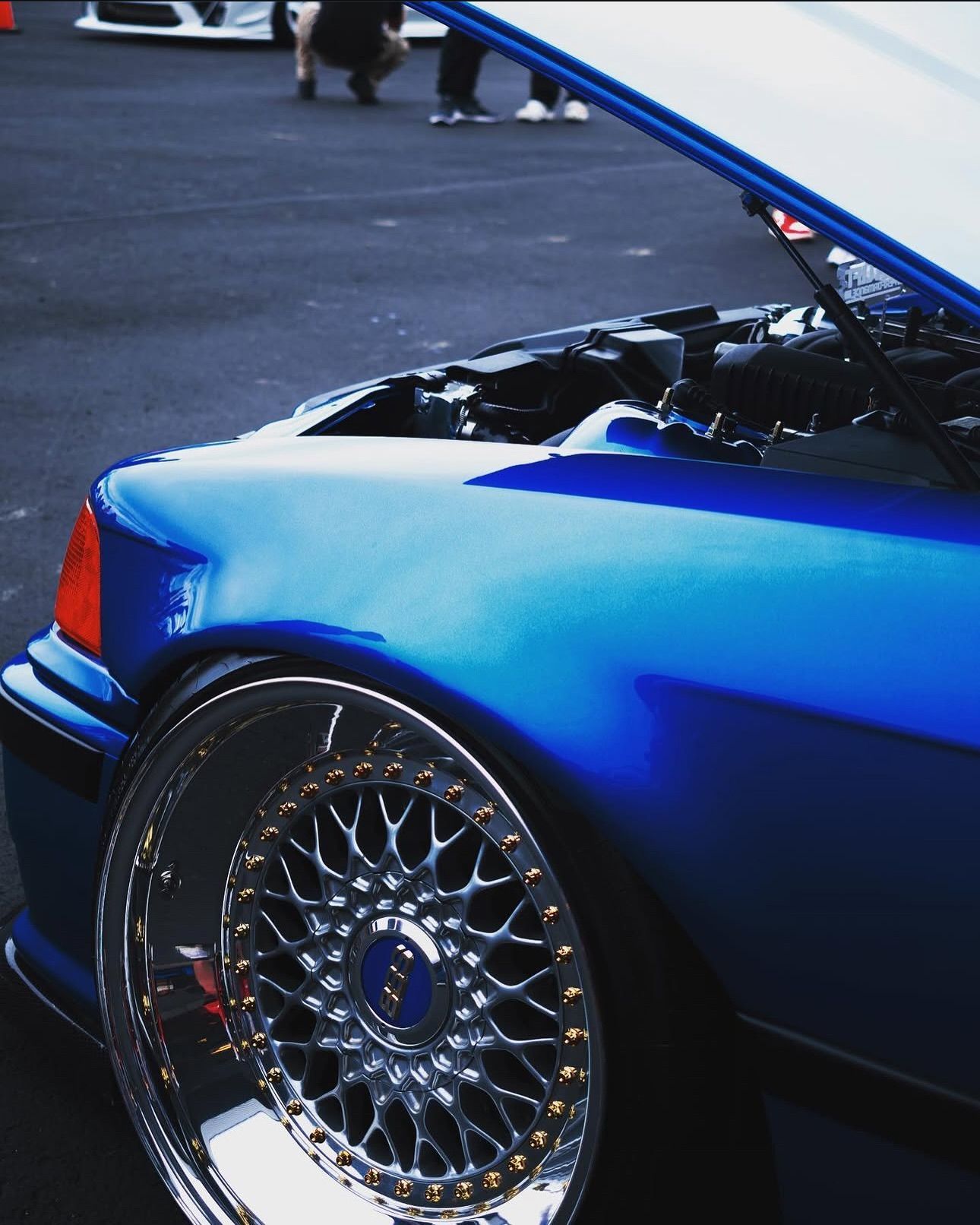 A blue car with the hood up is parked in a parking lot