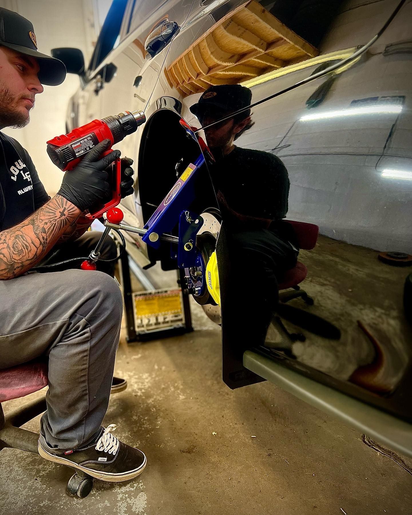 A man is using a drill to fix a car in a garage.