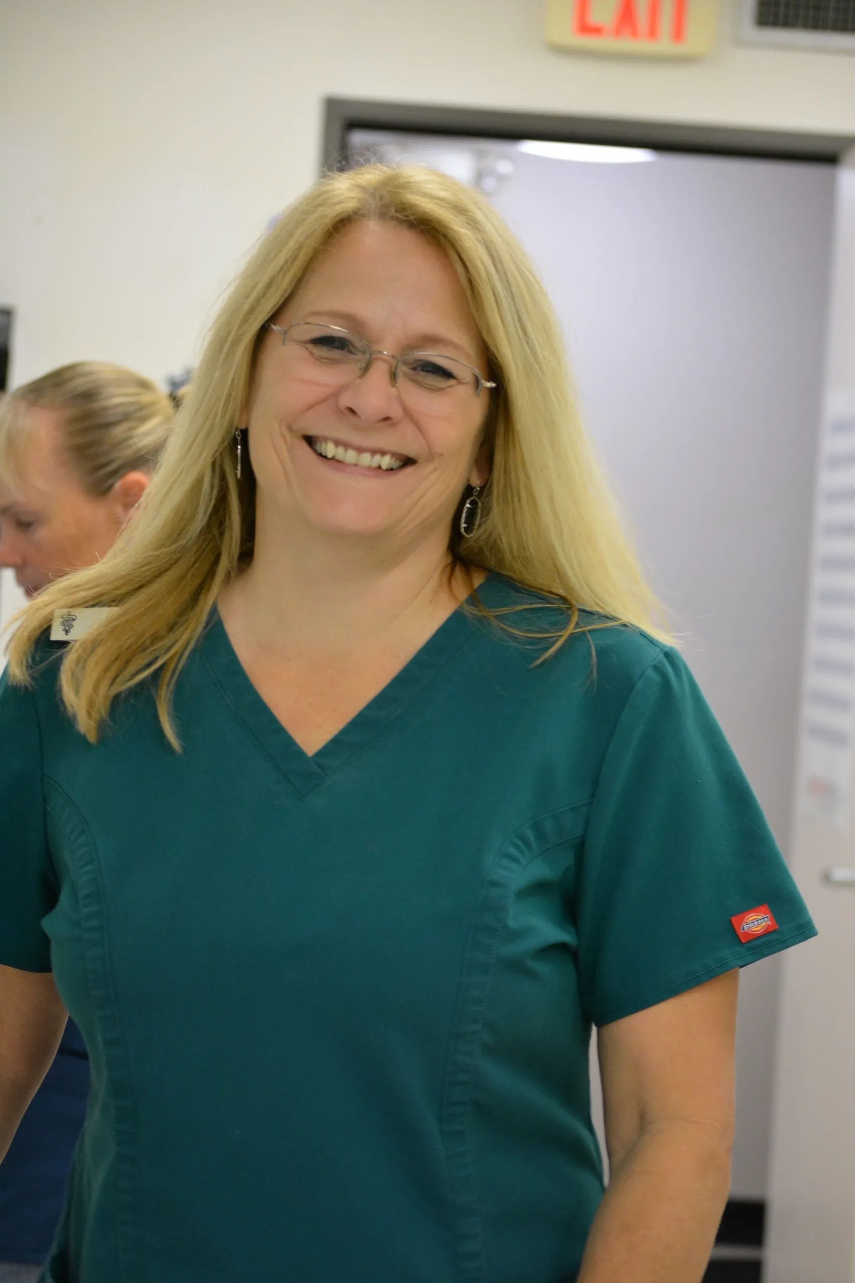 Smiling woman in teal scrubs standing in a hallway