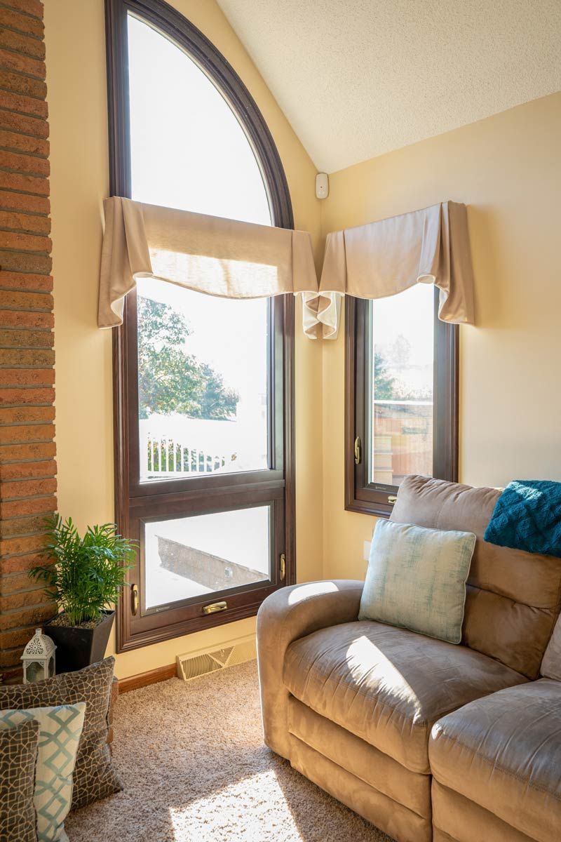 a living room with a couch , chair , and two windows .