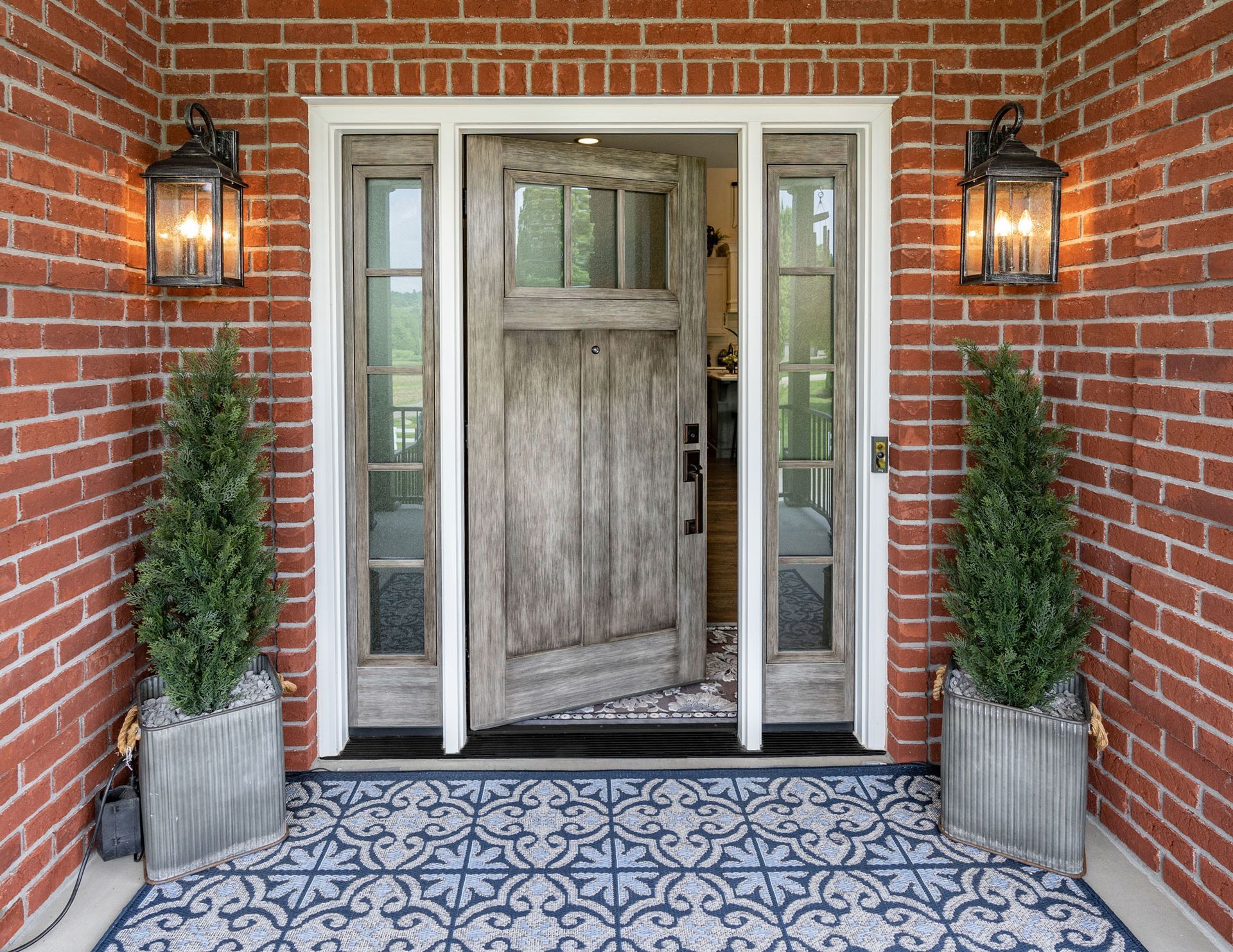 the front door of a brick house with a wooden door and two potted plants in front of it .