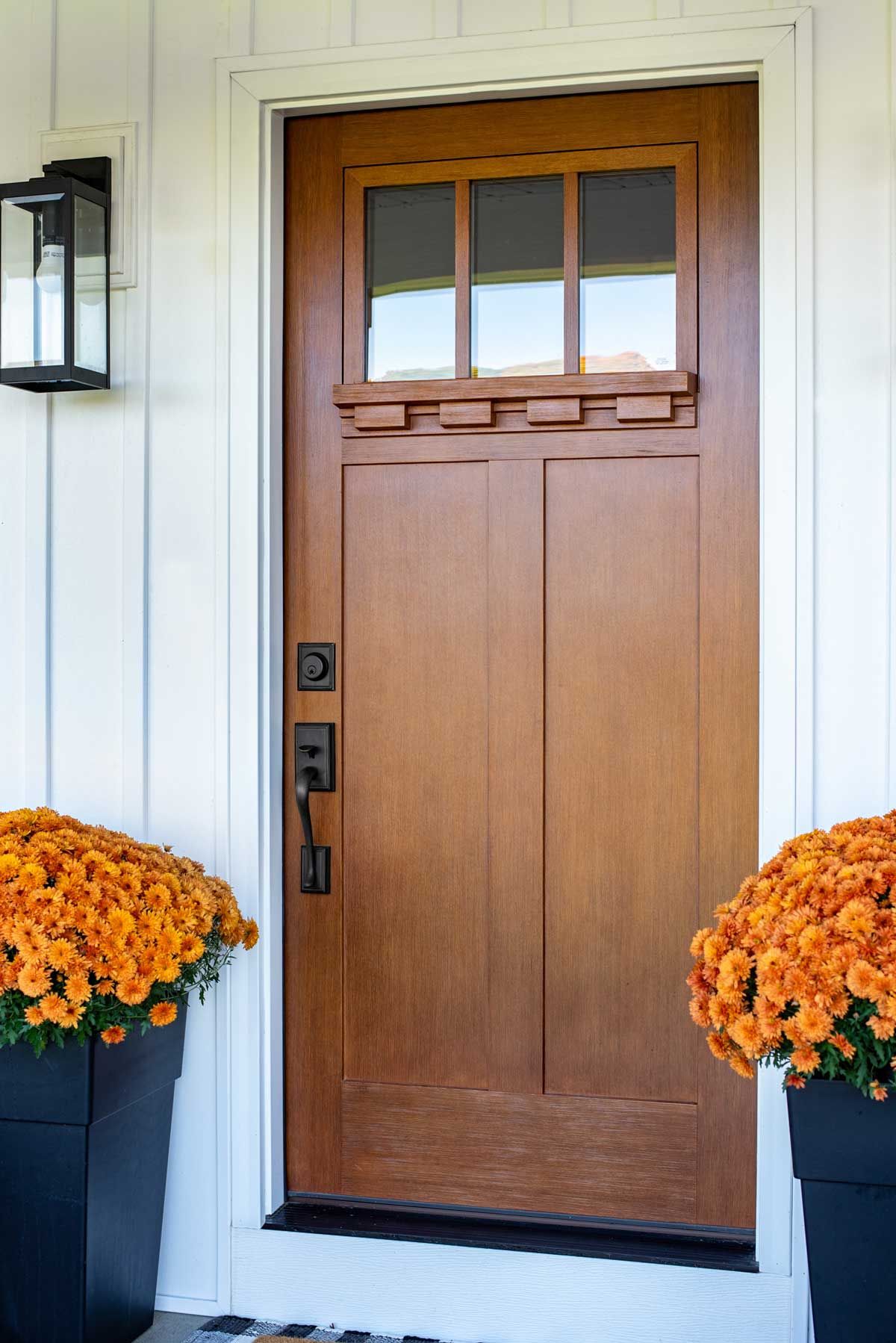 the front door of a house with a wooden door and two potted flowers in front of it .