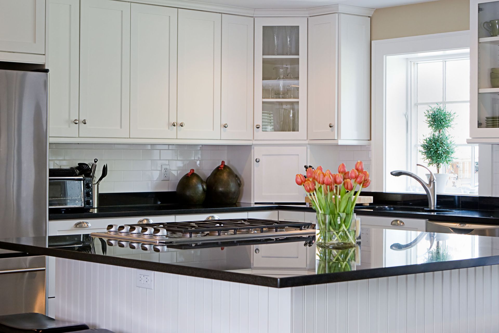 a kitchen with white cabinets and black counter tops and a vase of flowers on the counter