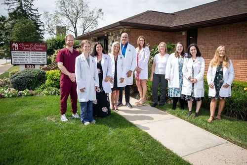 Medical staff in white coats and scrubs standing outside a brick building by a sidewalk