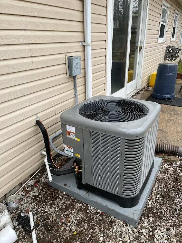 Outdoor central air conditioner unit beside a house wall on a concrete pad