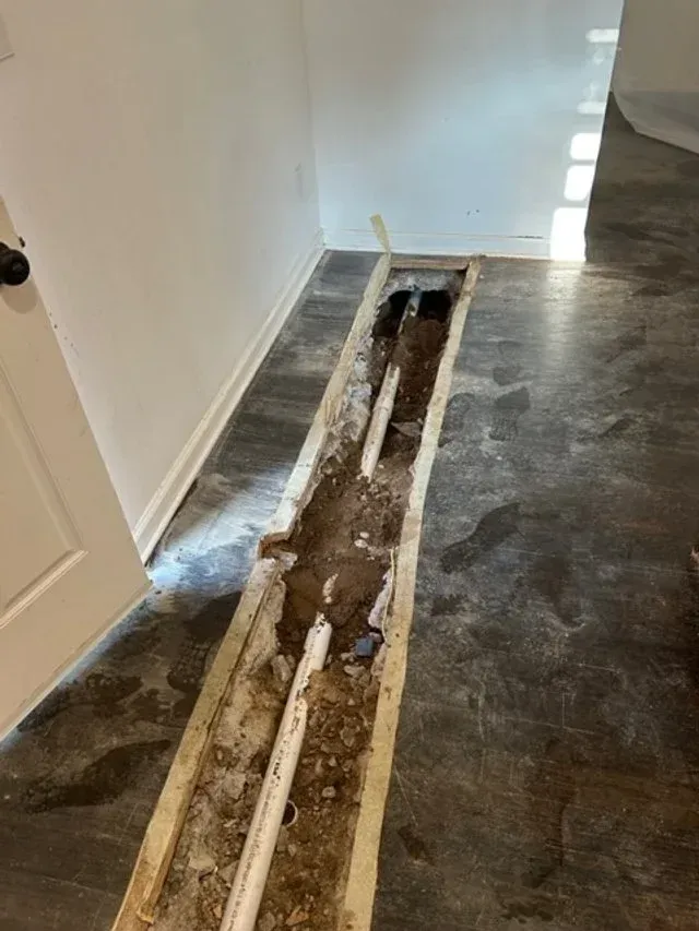 Open floor trench along a hallway with exposed pipes and concrete debris