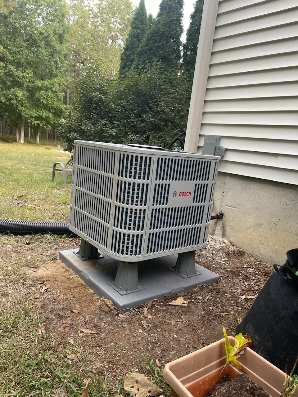 Outdoor central air conditioner unit beside a house on a gravel and mulch yard.