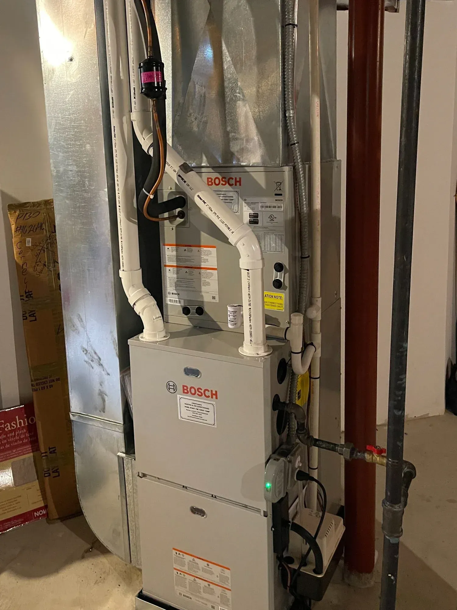Furnace and ductwork in a basement utility room with exposed pipes and metal venting.