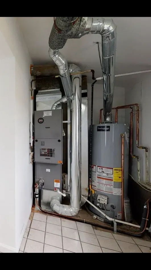 Utility room with water heater, furnace, and exposed ductwork and pipes on tiled floor