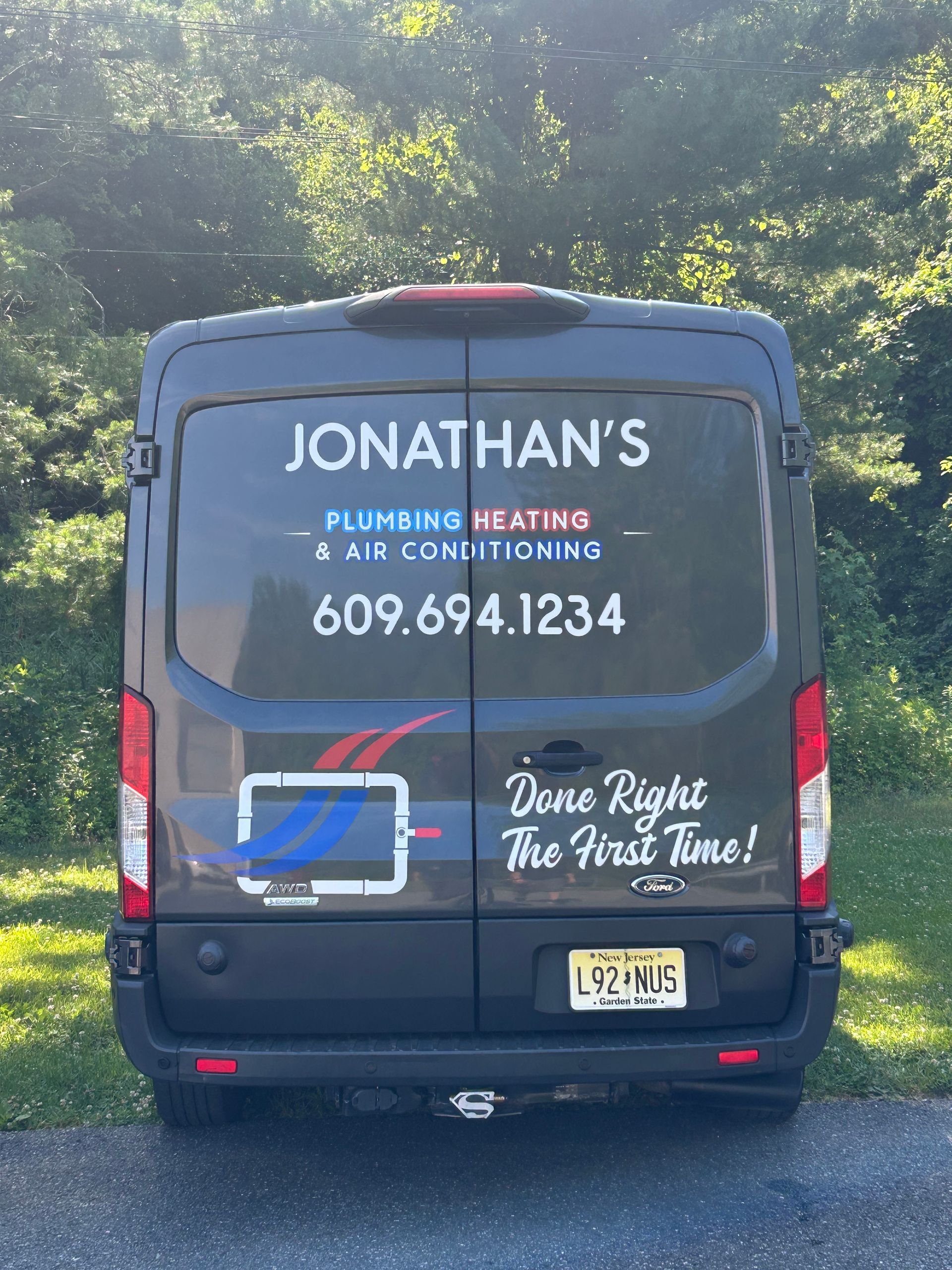 Workers and vans parked on a gravel lot beside trees under a blue sky