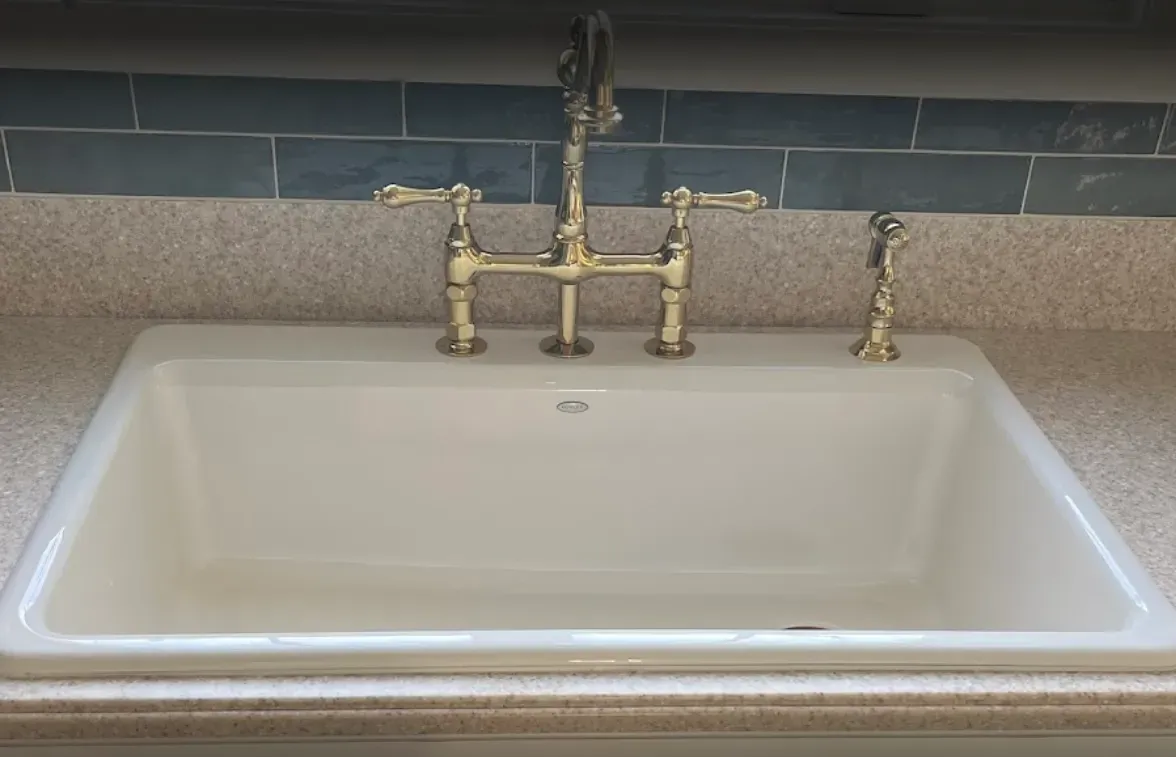 Kitchen sink with brass faucet and side sprayer against a gray tile backsplash