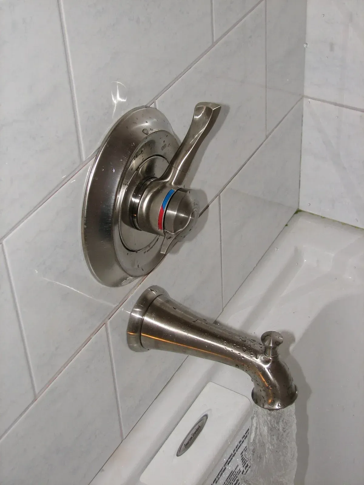 Chrome bathtub faucet and shower control mounted on white tiled bathroom wall