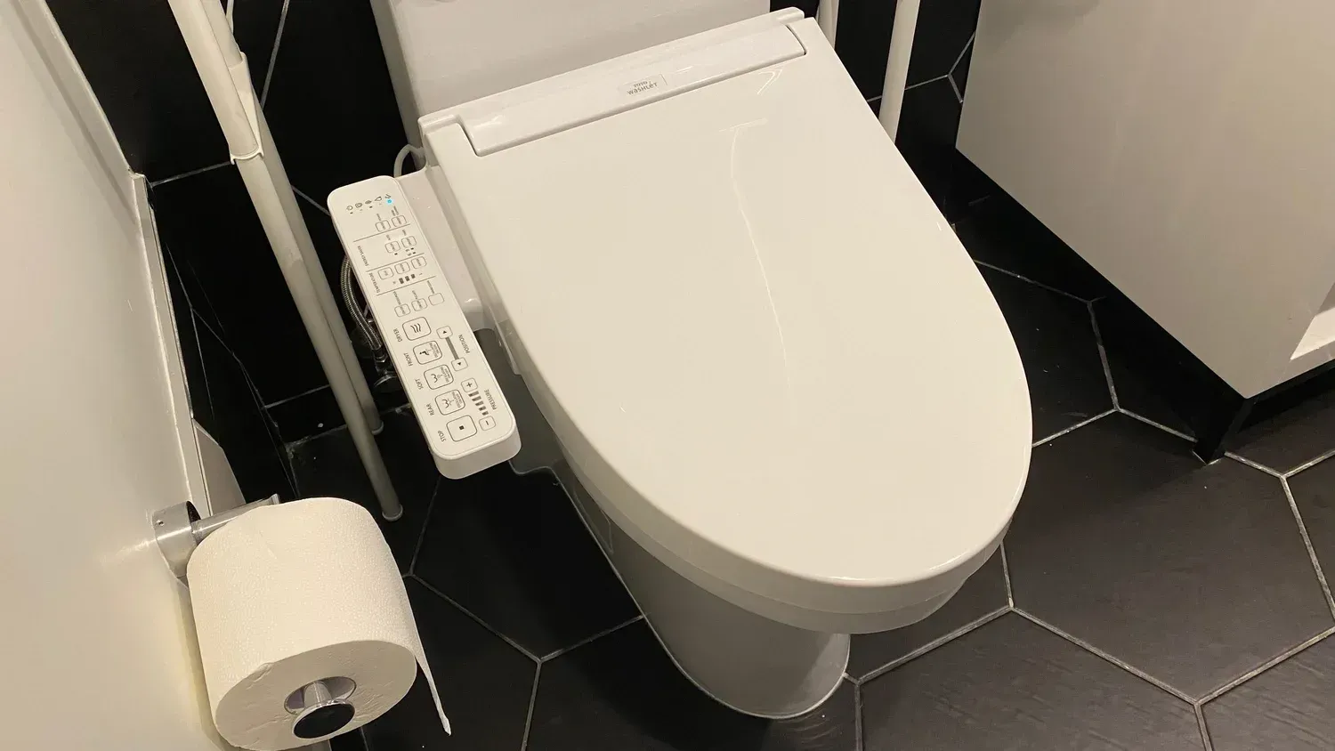 Modern toilet with bidet in a tiled bathroom, with a toilet paper holder beside it.