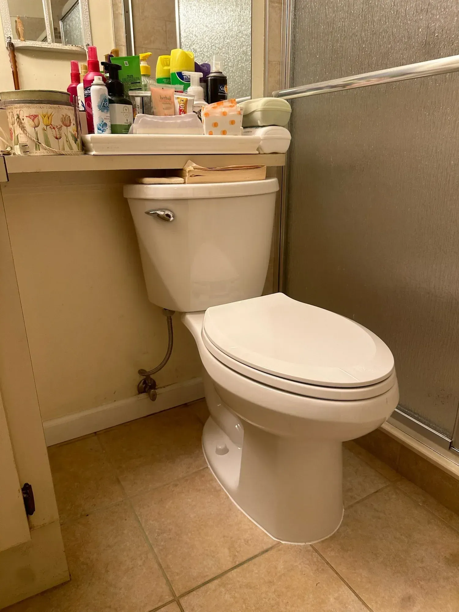 Small bathroom with a white toilet beneath a cluttered sink counter and beige tiled walls.