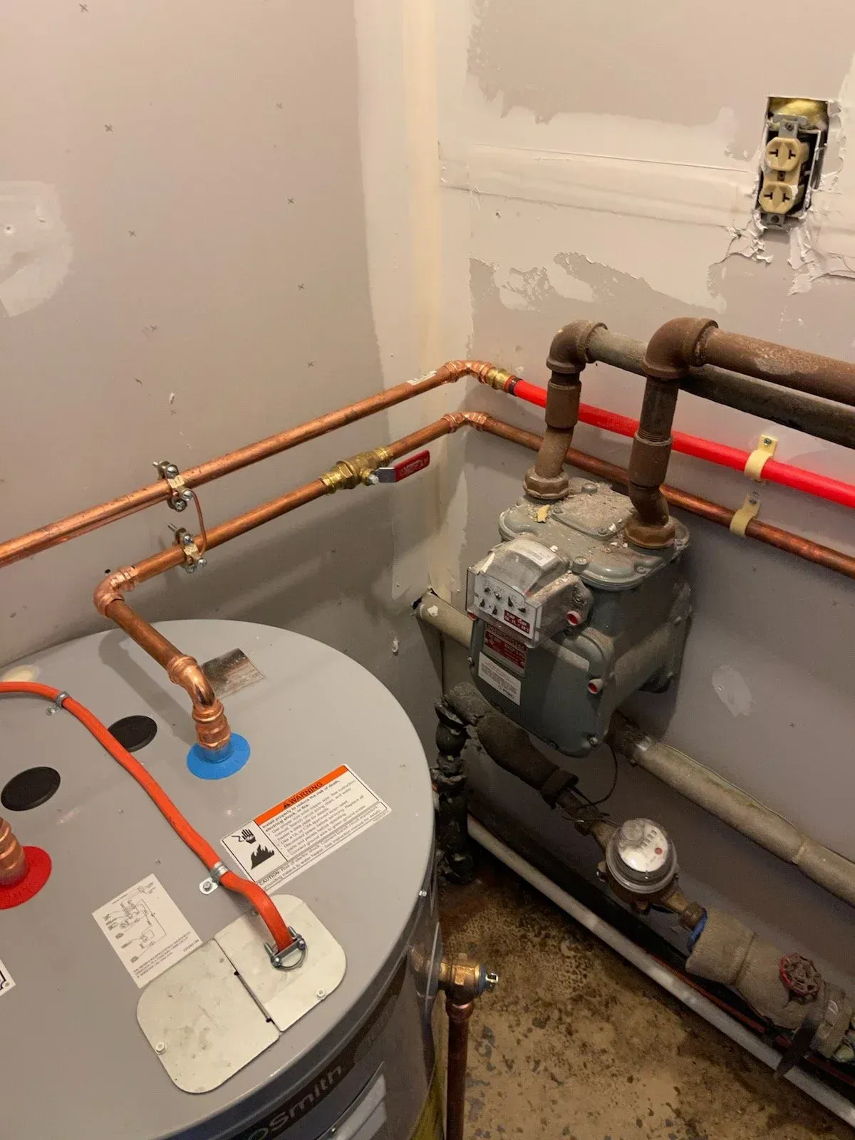 Basement utility room with water heater, pump, and copper pipes along the wall.