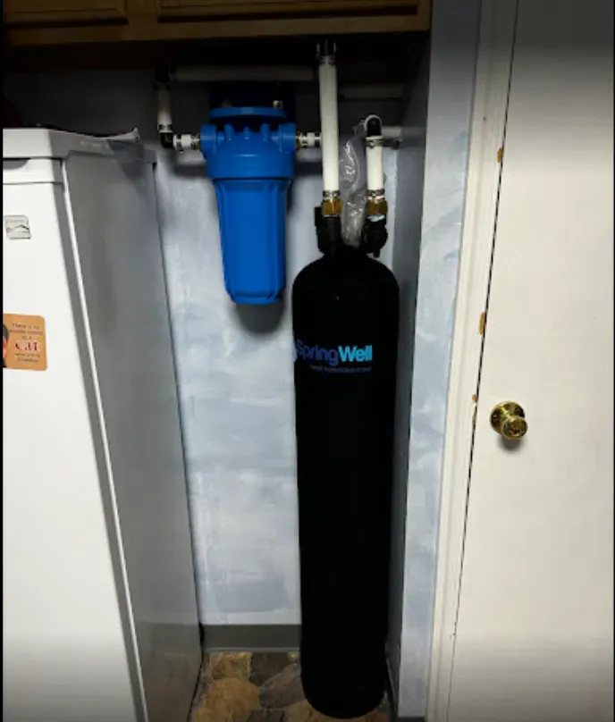 Water softener and blue filter tank installed in a utility closet beside a door.