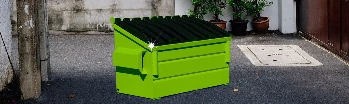 Bright green dumpster on asphalt, between stone wall and brown wooden door. Plants in background.