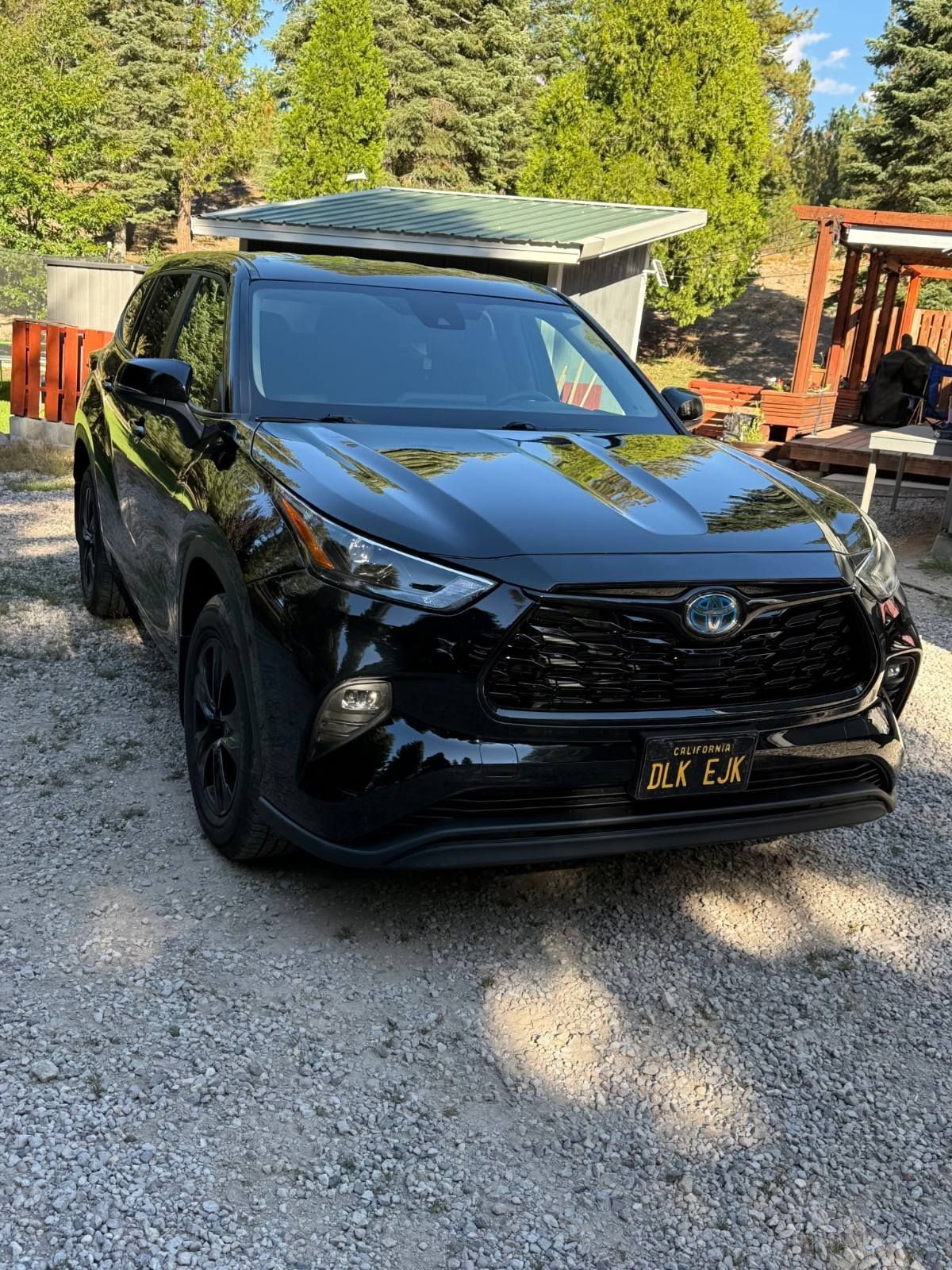 Black SUV parked on a gravel driveway with trees and a small shed in the background.