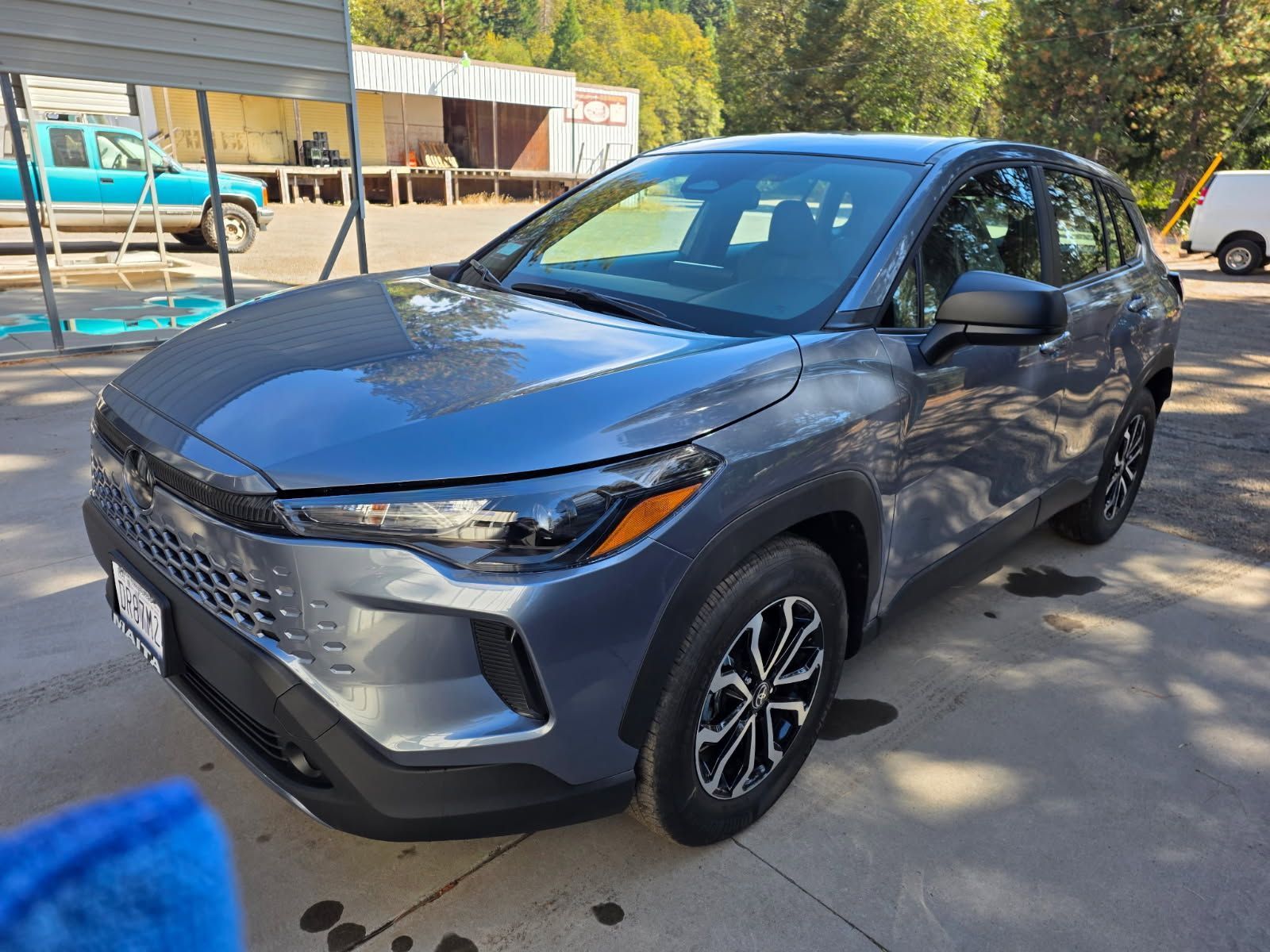 Blue-gray SUV parked outdoors in a lot, front-left view, with a building and trees in the background