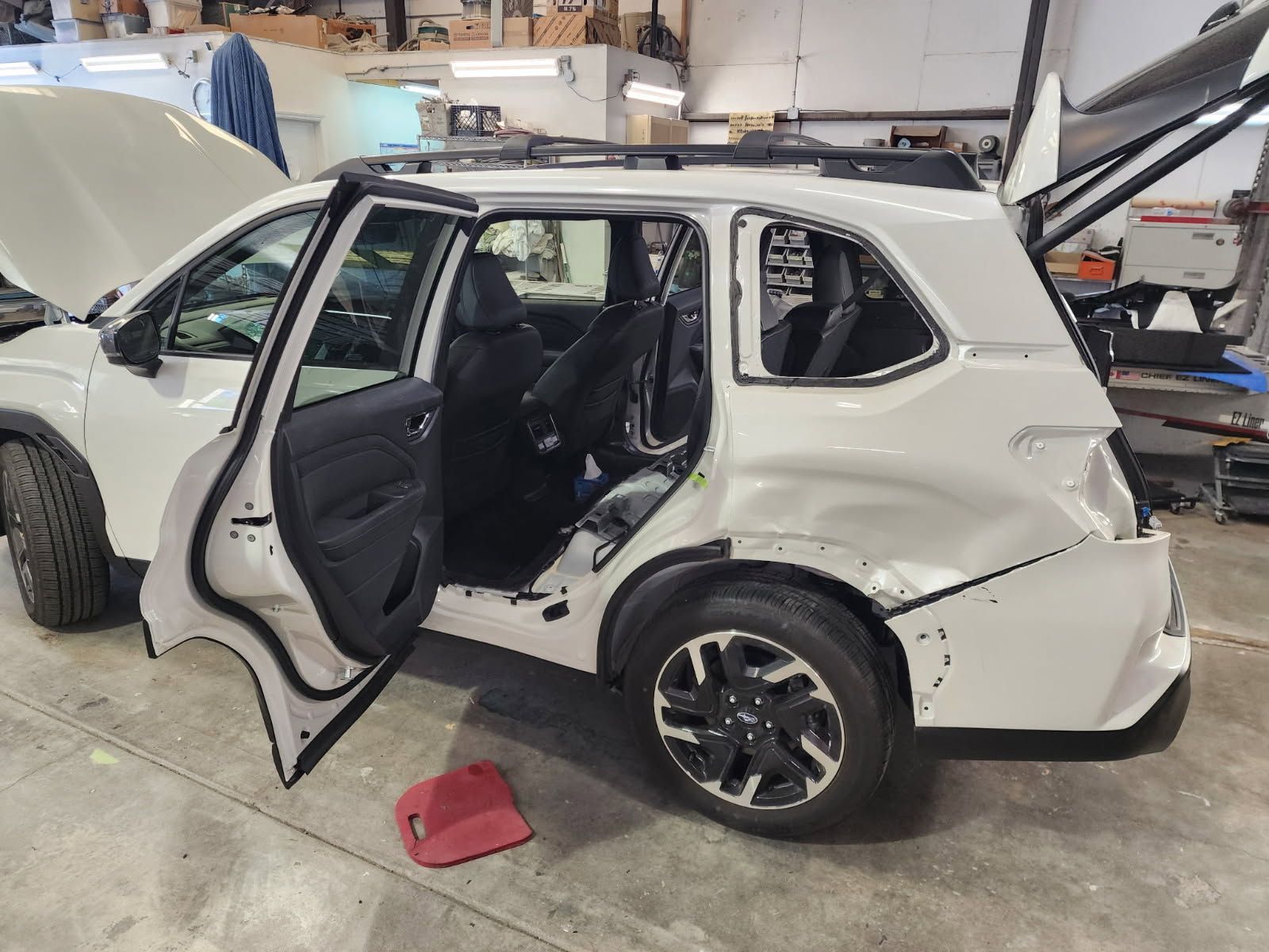Damaged white SUV in an auto repair shop with doors open and rear side heavily dented