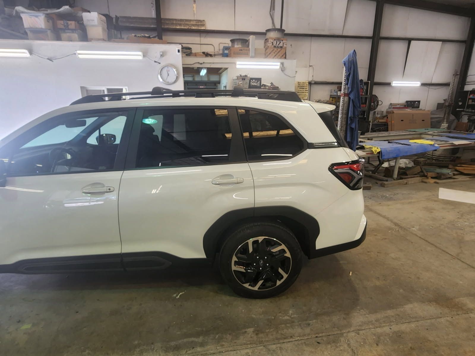 White SUV in a workshop garage, side view with black roof and wheels.