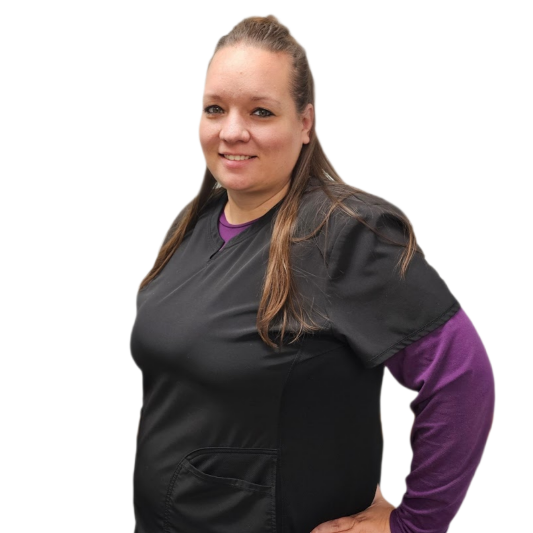 Woman in black scrubs with purple long-sleeve shirt underneath, smiles in front of a gray wall.