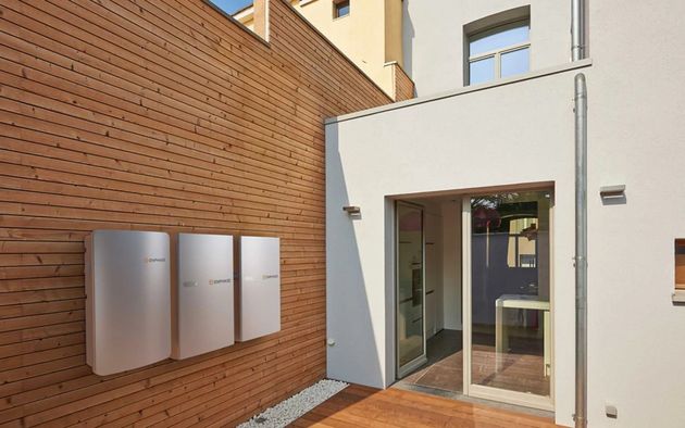 Modern courtyard entrance beside brick wall and mailboxes, with open glass door and white building facade.