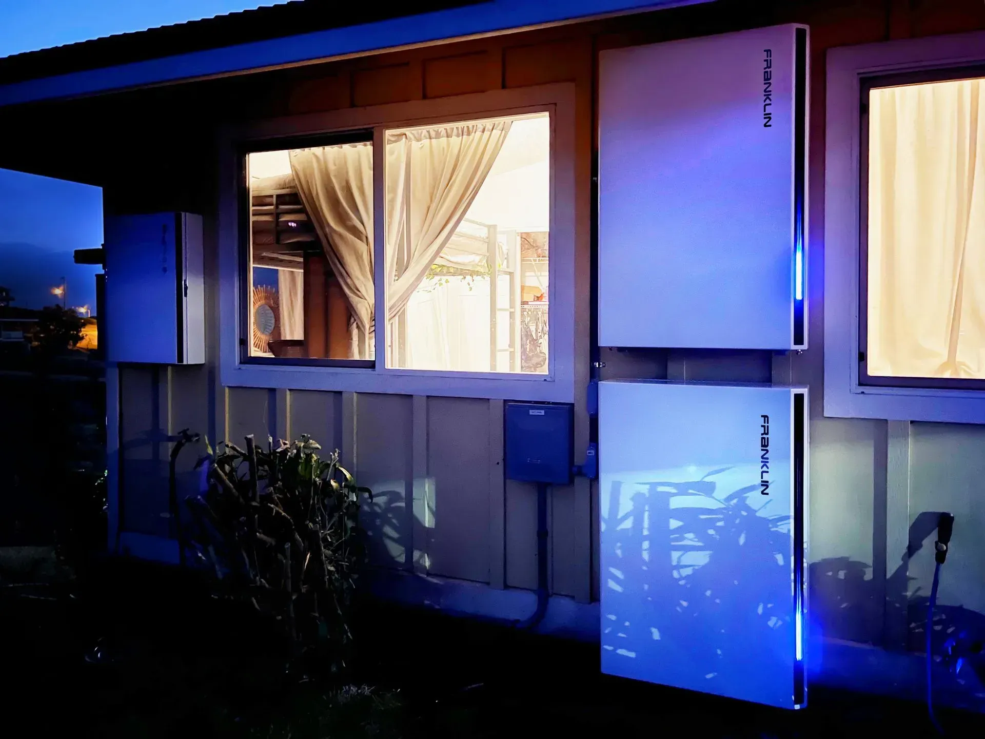 Blue-lit house exterior with curtained windows and illuminated wall panels at dusk