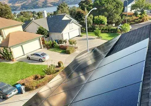 Suburban rooftops with solar panels, a driveway, and green landscaped homes on a sunny day